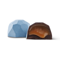 Two faceted gourmet chocolates on a white background, with one whole chocolate in light blue and one cut open showing a caramel-colored filling.