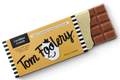 A single wrapped chocolate bar on a clean white background. The wrapper is tan with black-and-white striped edges, large 'Tom Foolery' script, and 'Cornflake Crunch' text.